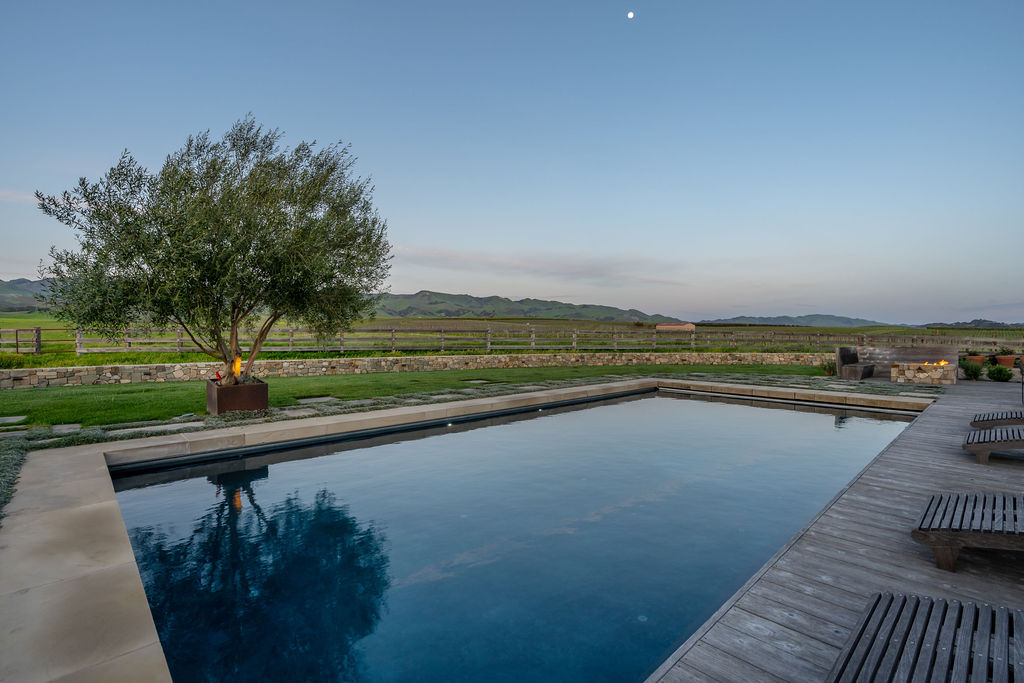 The Vineyard House pool at dusk, moon overhead and fire pit glowing beyond