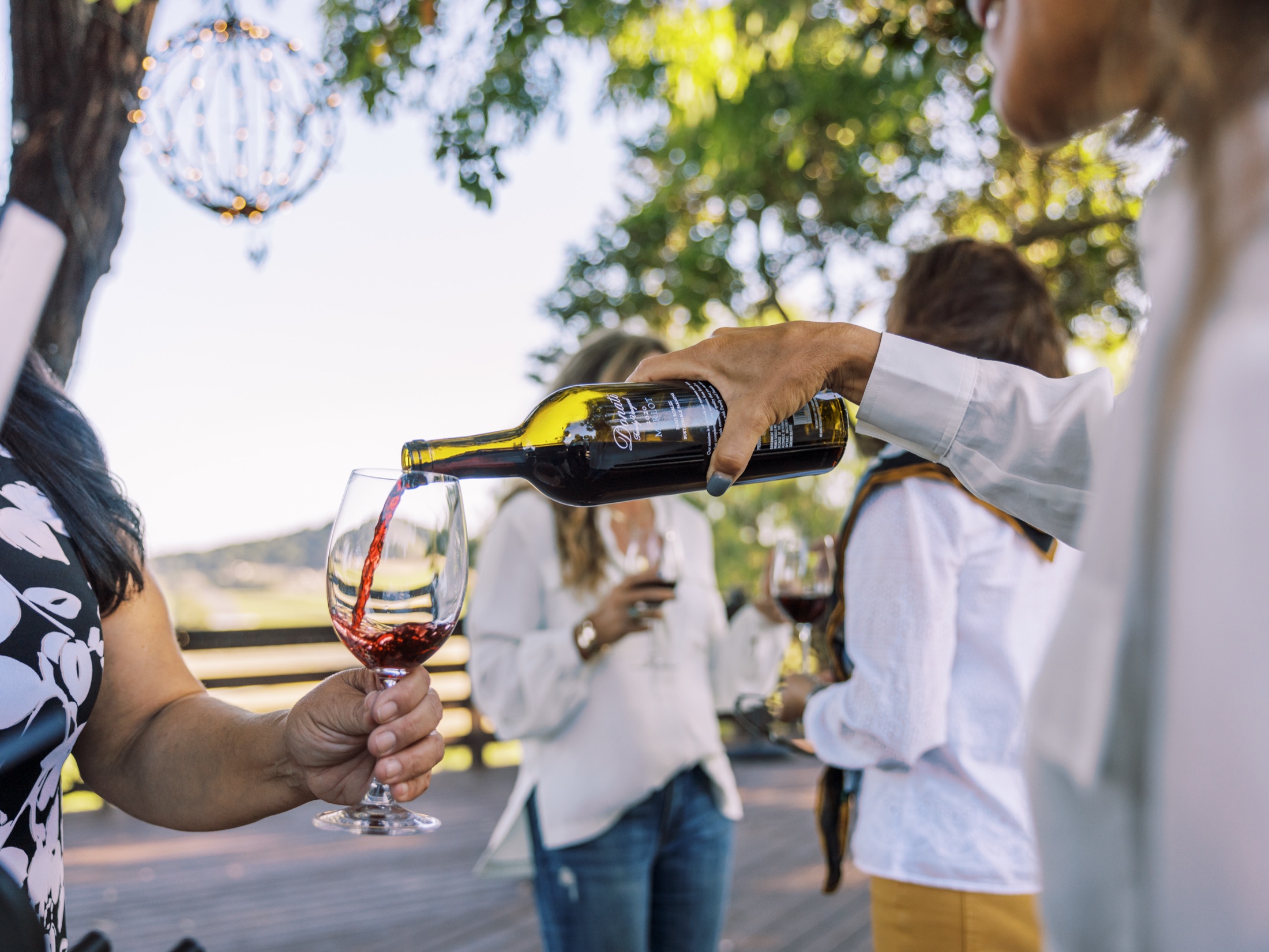 A glass of red wine being poured outdoors beneath the trees at Cavalli